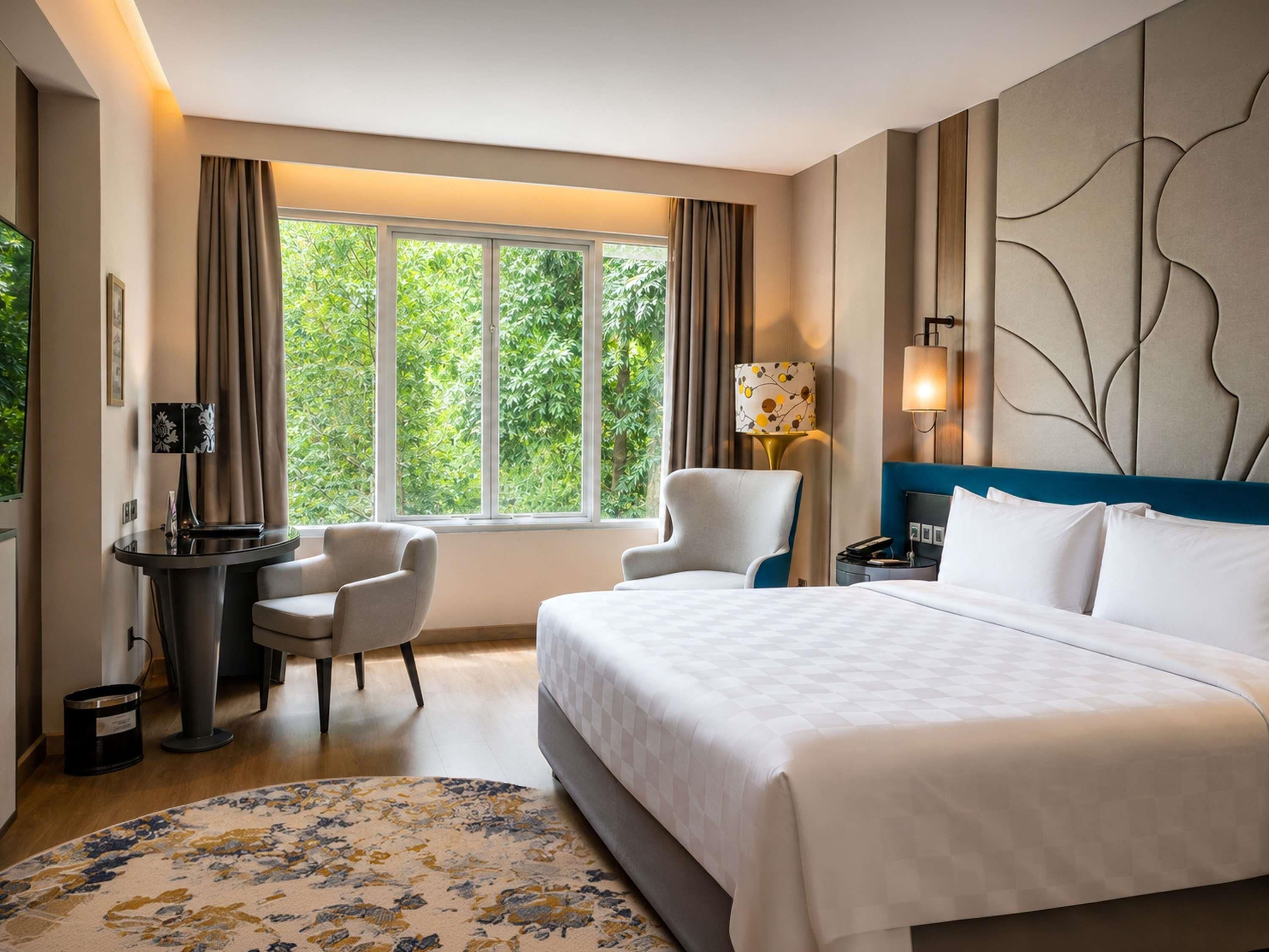 Ein Hotelzimmer mit einem Bett, zwei Sesseln, einem Schreibtisch und einem großen Fenster mit Vorhängen.