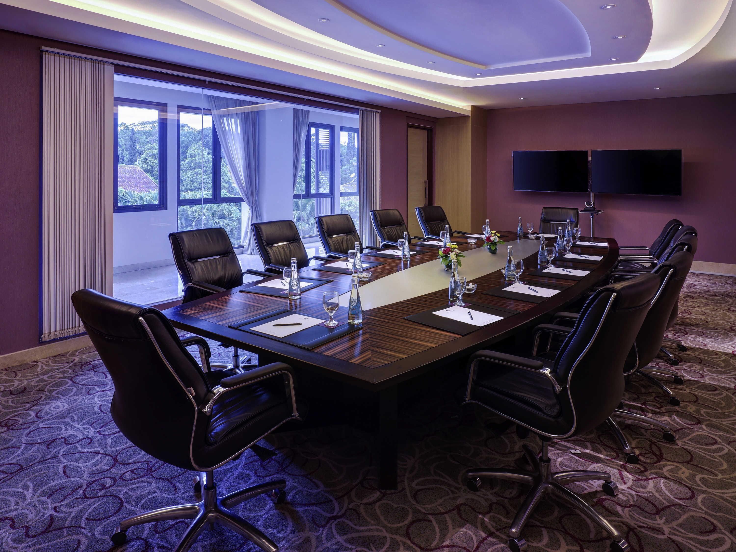 Un salón de conferencias con una larga mesa, sillas y una pantalla de televisión.