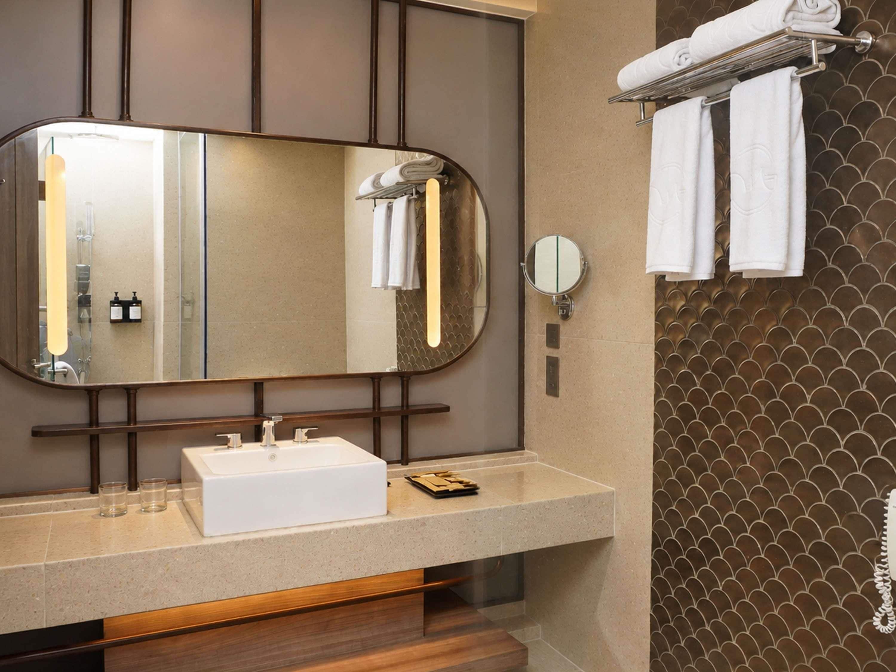 A bathroom with a large mirror, a white sink, a towel rack, and a wall with a fish-scale pattern.