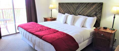 A neatly made bed with a red and white bedspread, two bedside lamps, a wooden headboard, and a small wooden nightstand with a remote control.