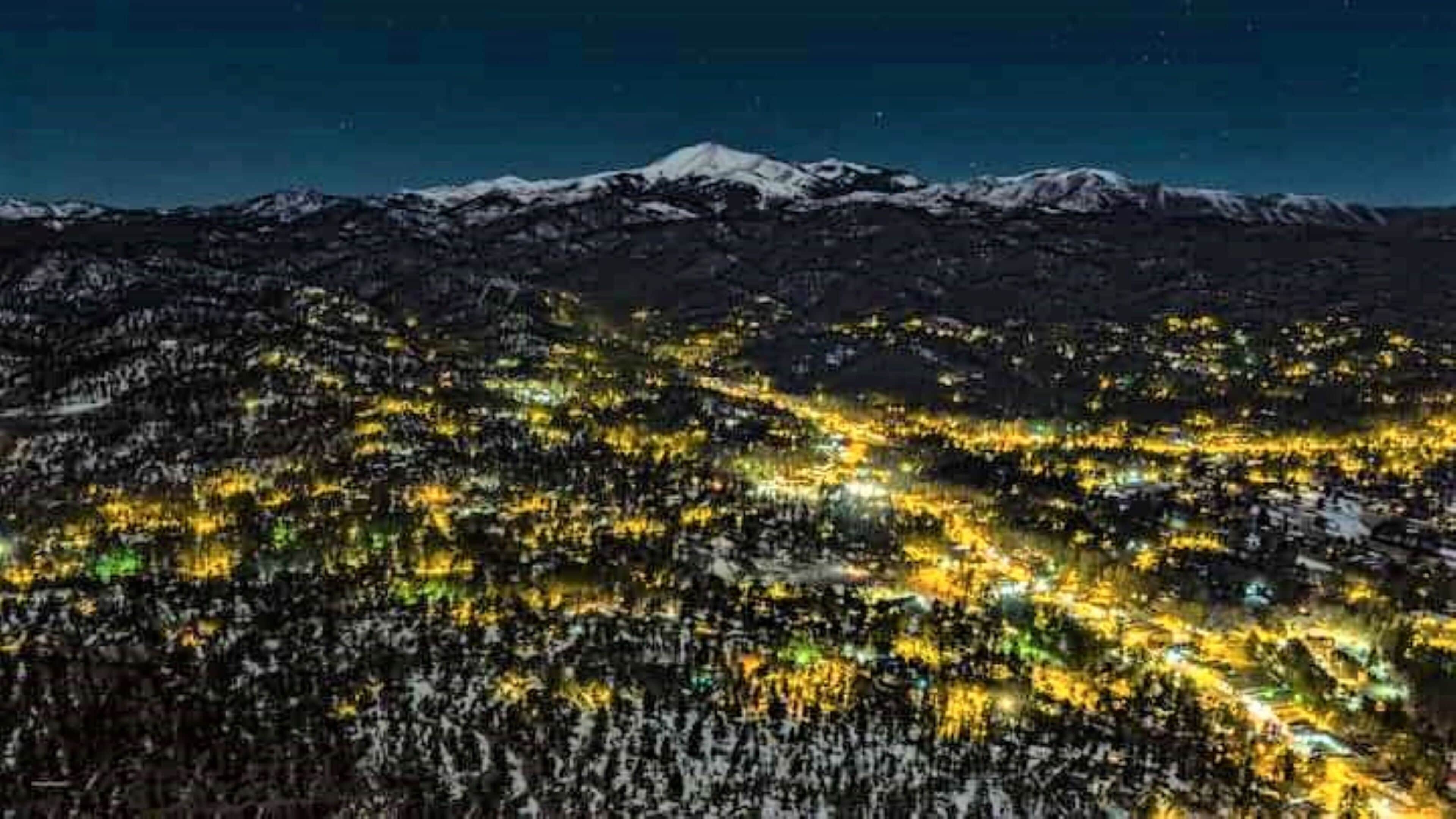 Une vue nocturne d’une ville avec une montagne en arrière-plan.