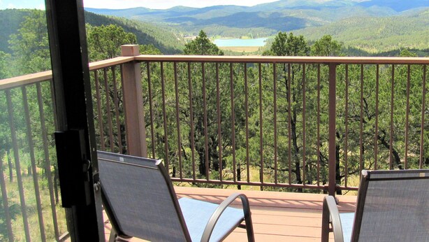 A balcony with two chairs overlooking a forested landscape and a lake. - High Sierra Condominium (Ruidoso)