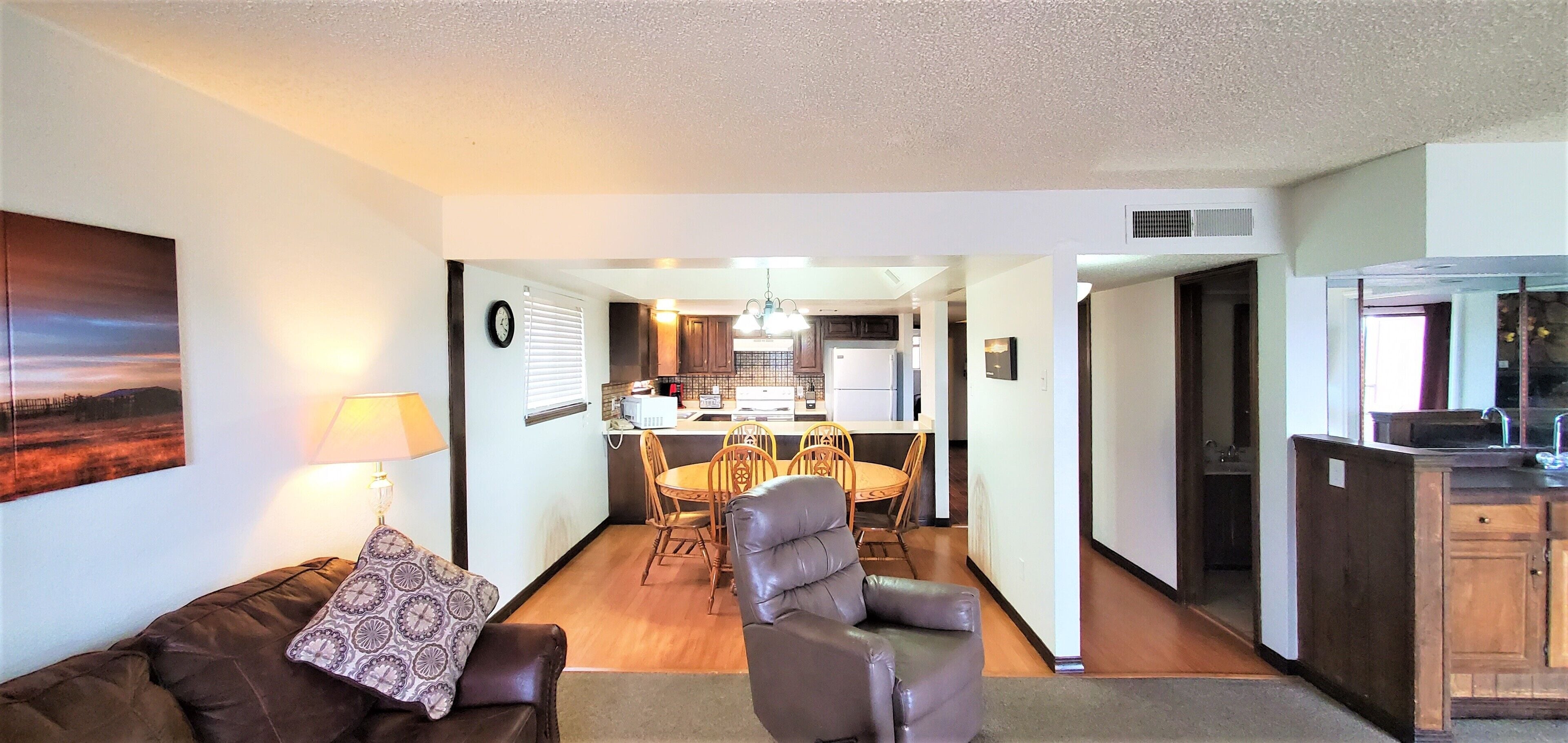 A living room with a sofa, a chair, a dining table with chairs, and a kitchen area with cabinets and a refrigerator.