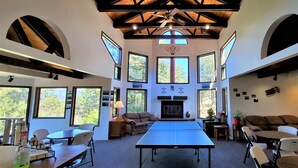 A spacious room with a ping pong table, seating area, large windows, and a fireplace. - High Sierra Condominium (Ruidoso)