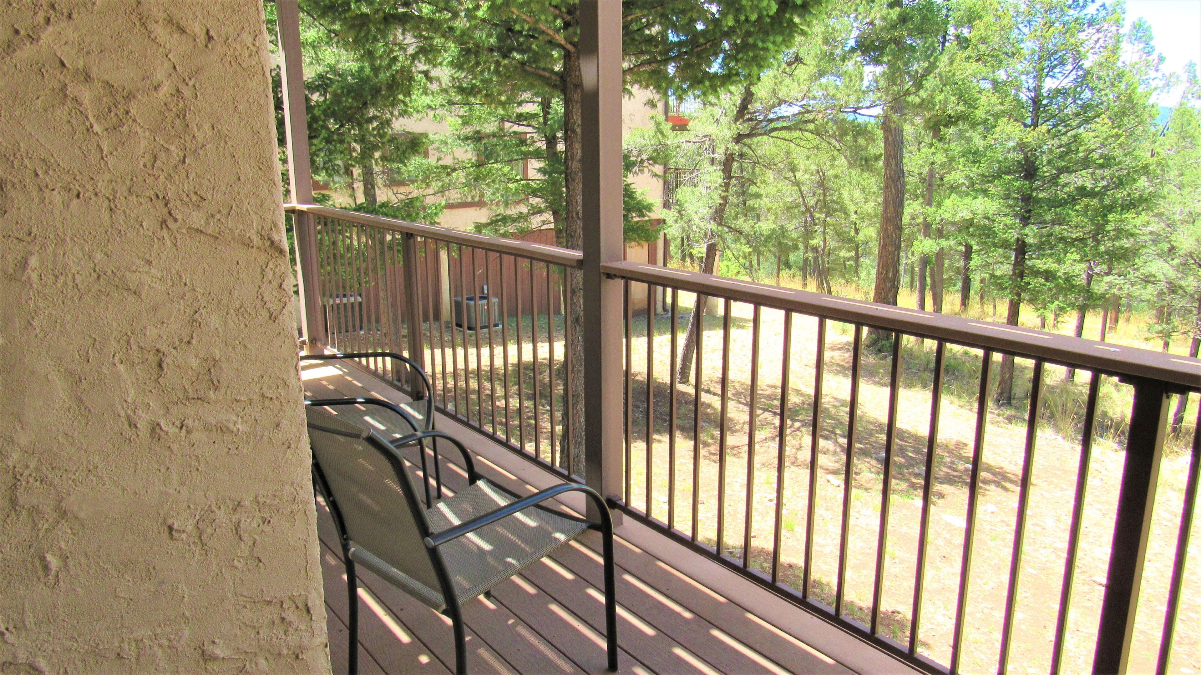 A wooden deck with metal railings, a bench, and a view of a wooded area.