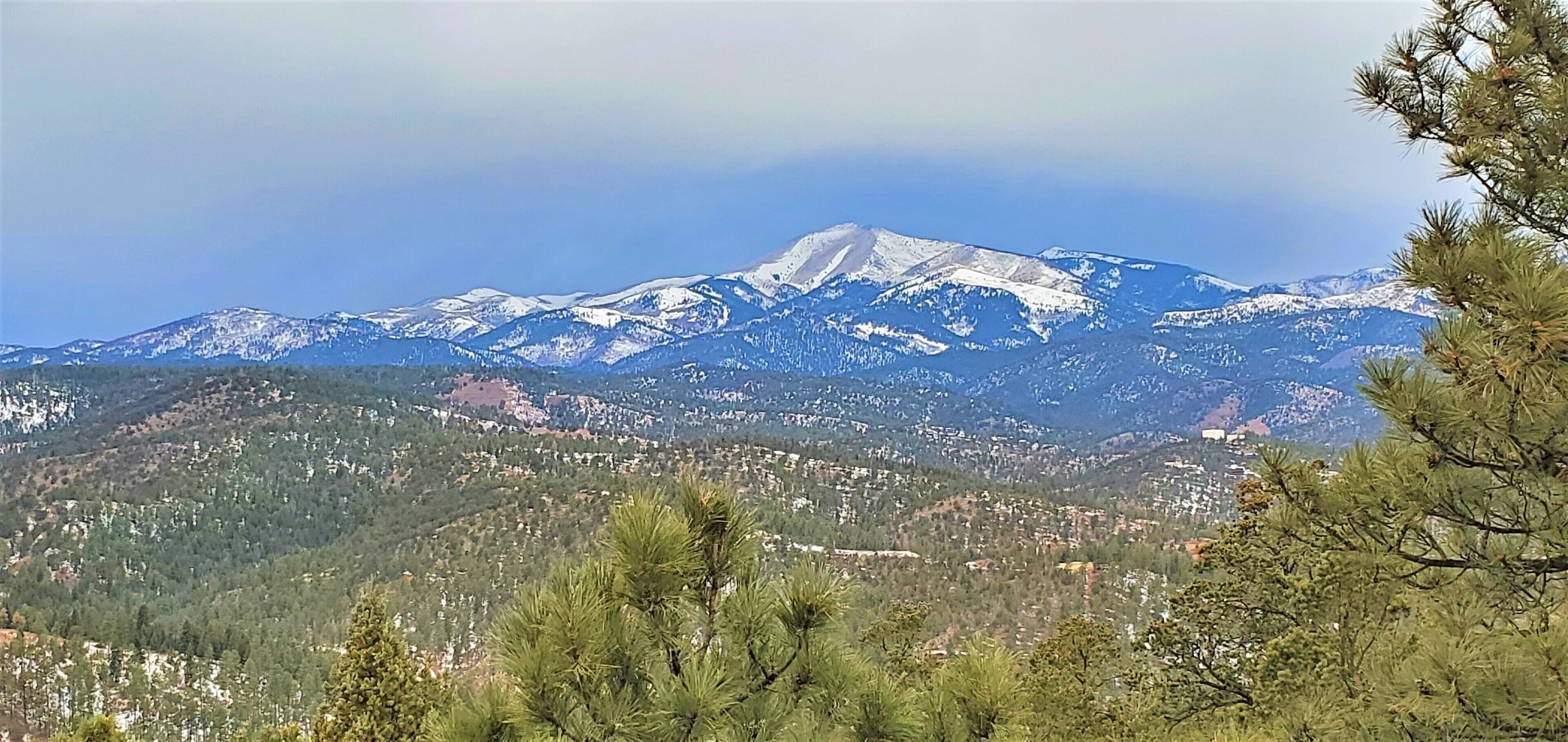 Una montaña con cumbres nevadas, un valle cubierto de bosque y un pueblo en primer plano.