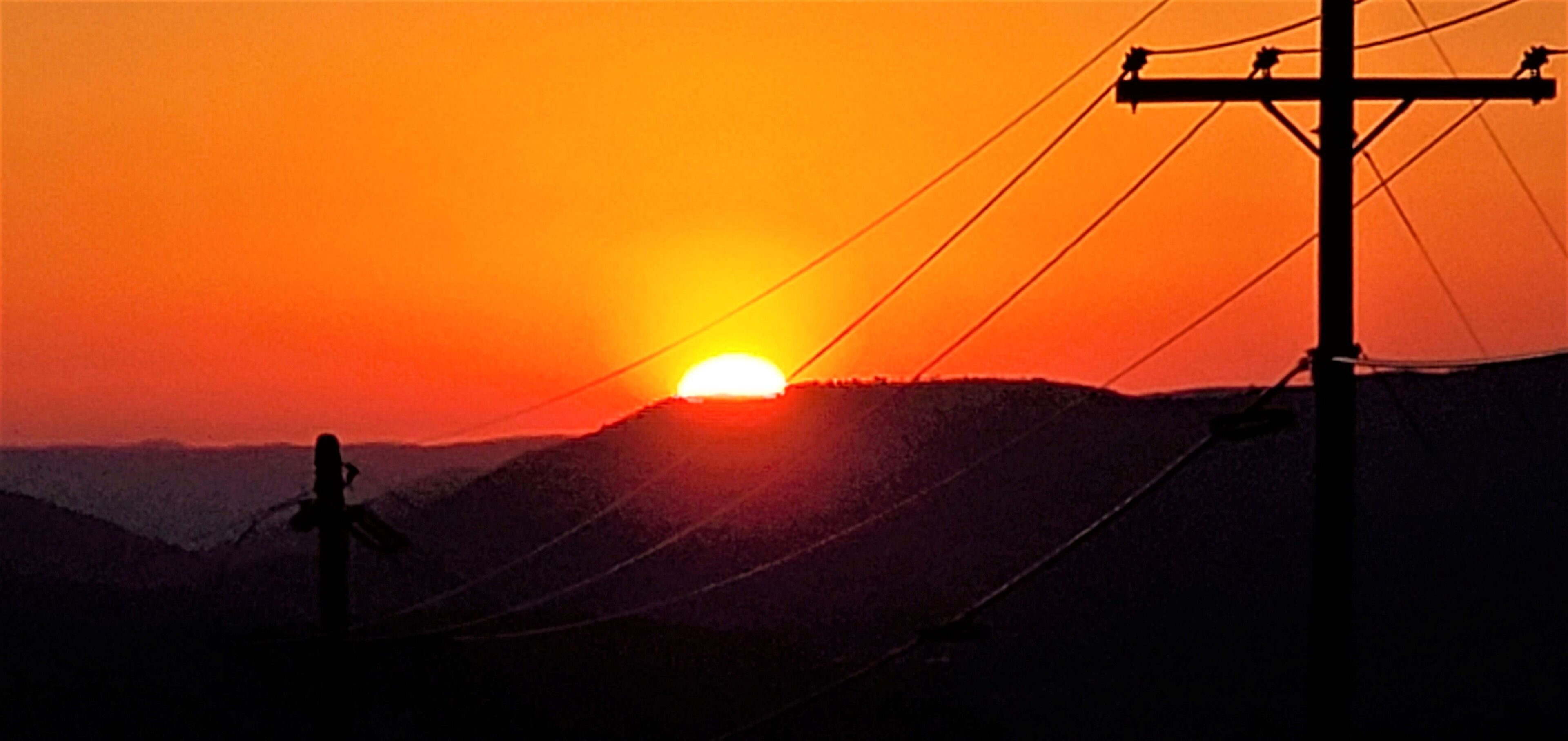 A sunset with a silhouette of a mountain and a utility pole.