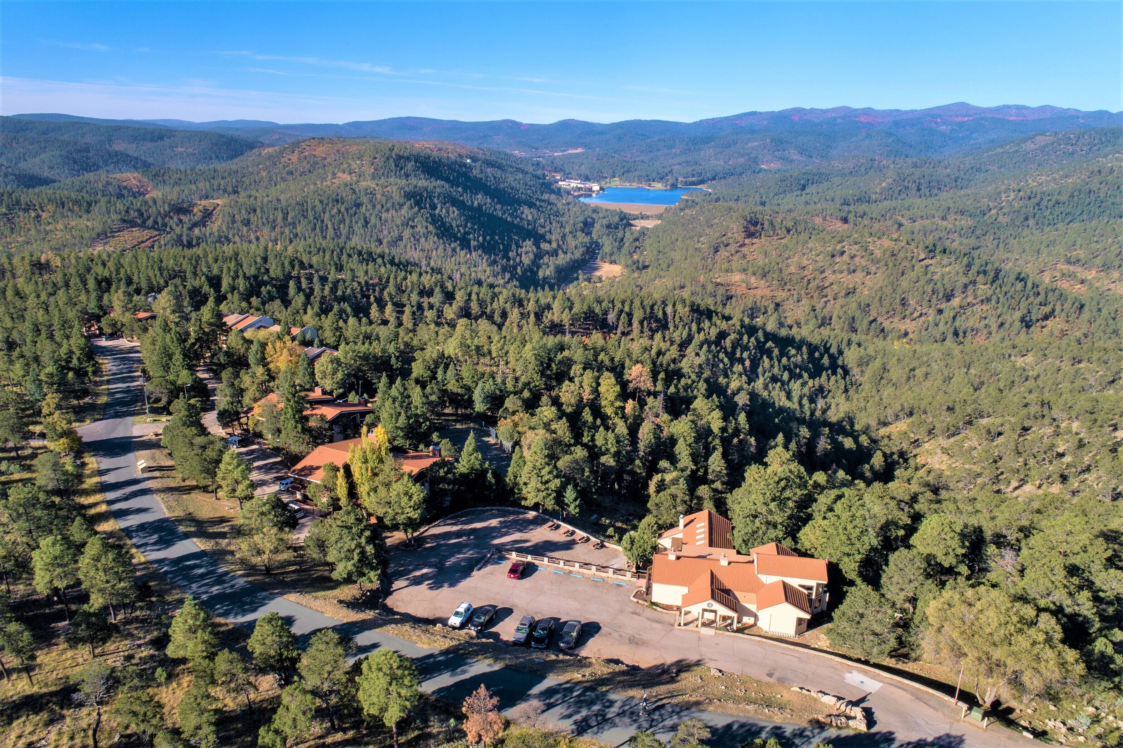 An aerial view of a resort with a parking lot, buildings, and a lake surrounded by forested hills.
