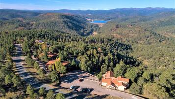 An aerial view of a resort with a parking lot, buildings, and a lake surrounded by forested hills.