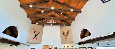 Una habitación con techos altos, vigas de madera y decoración con motivos de esquí, además de un ventilador de techo.