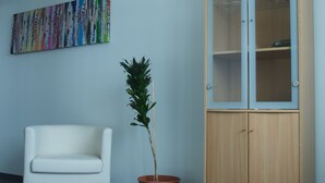 A room with a white sofa, a wooden cabinet, a potted plant, and a colorful abstract painting on the wall. - Grundarfjördur Hostel (Grundarfjörður)
