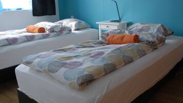 Hotellihuone, jossa on kaksi erillistä sänkyä, jokaisessa kuviollinen peitto ja tyynyt, yöpöytä lampun kanssa sekä ikkuna, jossa on verhot.