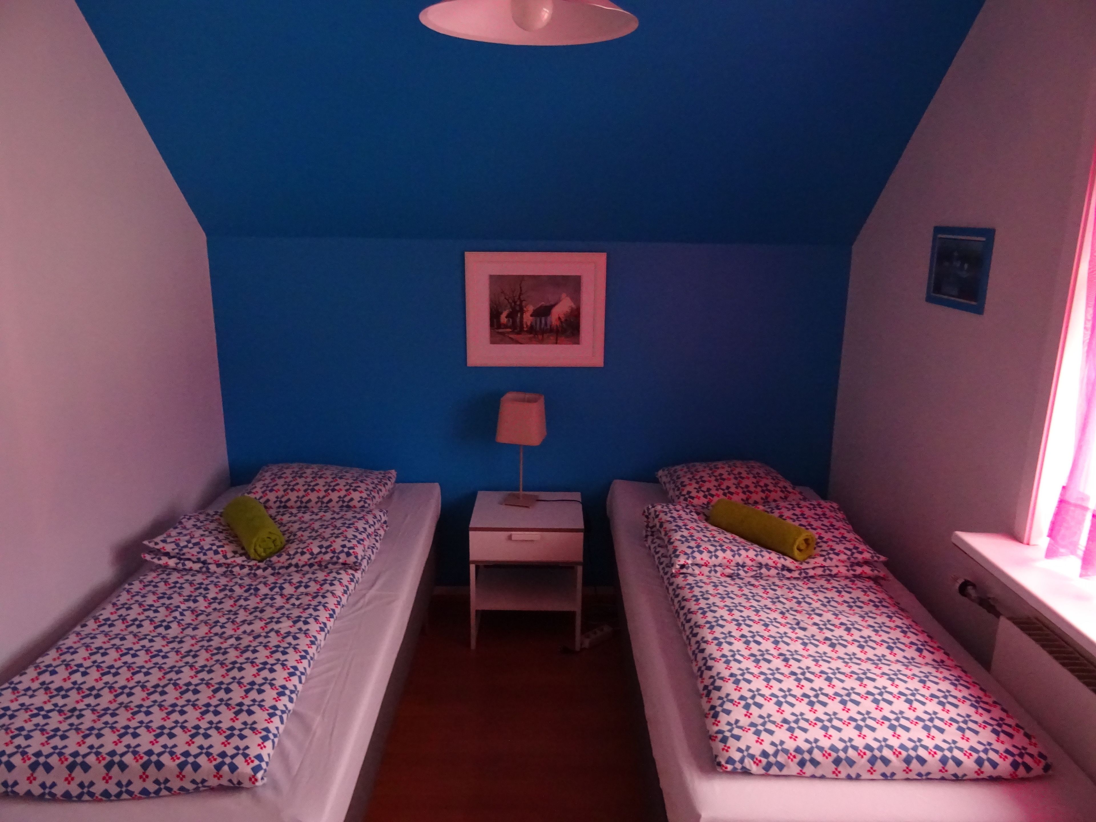 Una camera singola e piccola con due letti, un comodino, una lampada e un quadro appeso alla parete.