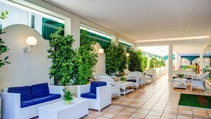 Un patio interior espacioso con mobiliario de mimbre blanco, plantas verdes y piso de baldosas.