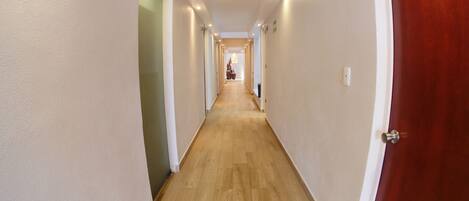 Een lange, smalle gang met houten vloer en witte wanden.