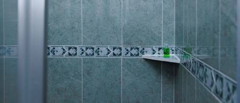 A shower with a handheld showerhead, a corner shelf, and a wall-mounted faucet.