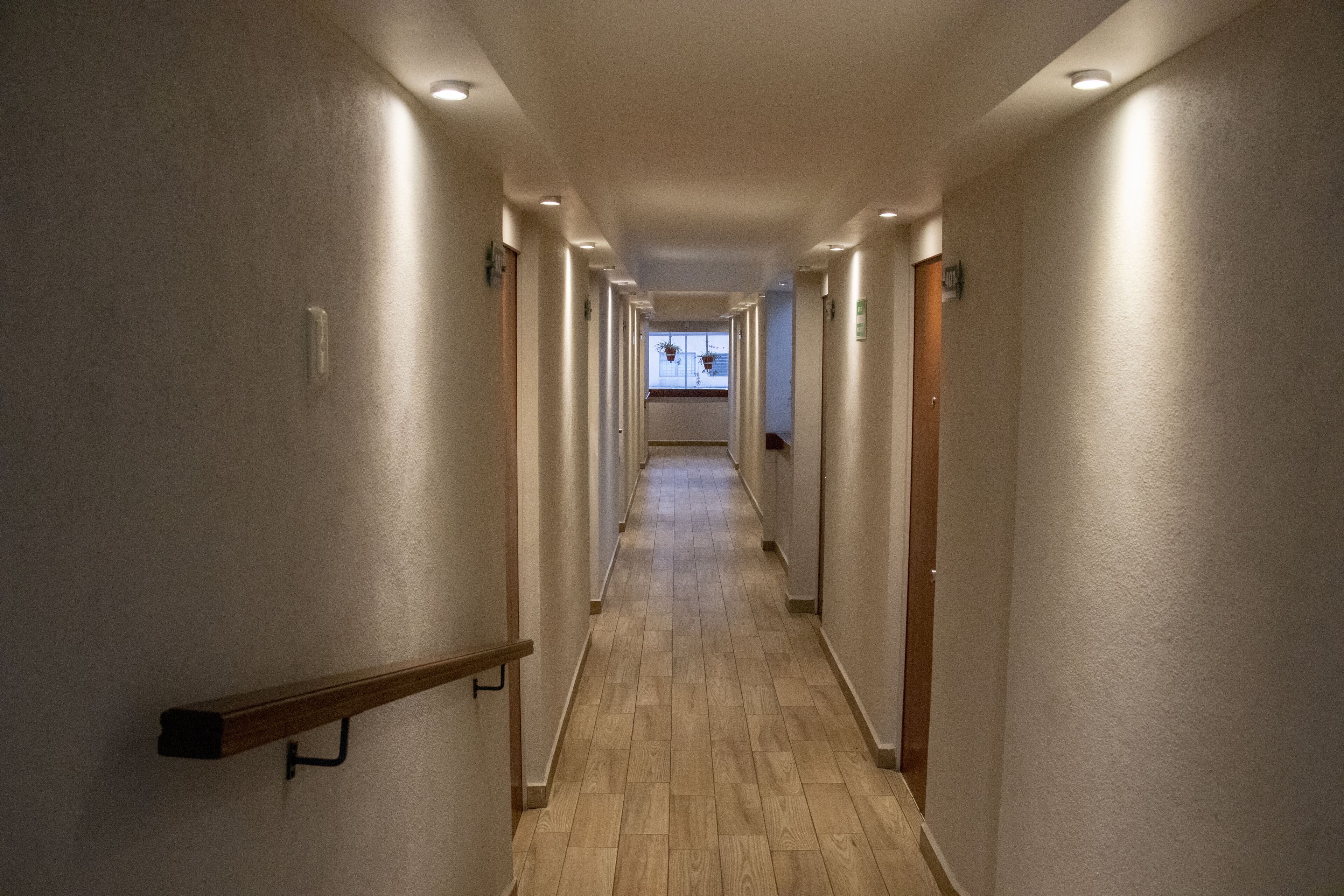 A long, narrow hallway with wooden flooring and white walls, leading to a door at the end.