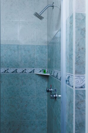 A bathroom with a shower, tiled walls, a shelf with toiletries, and a decorative border. - Hotel Qualitel Centro Histórico (Morelia)