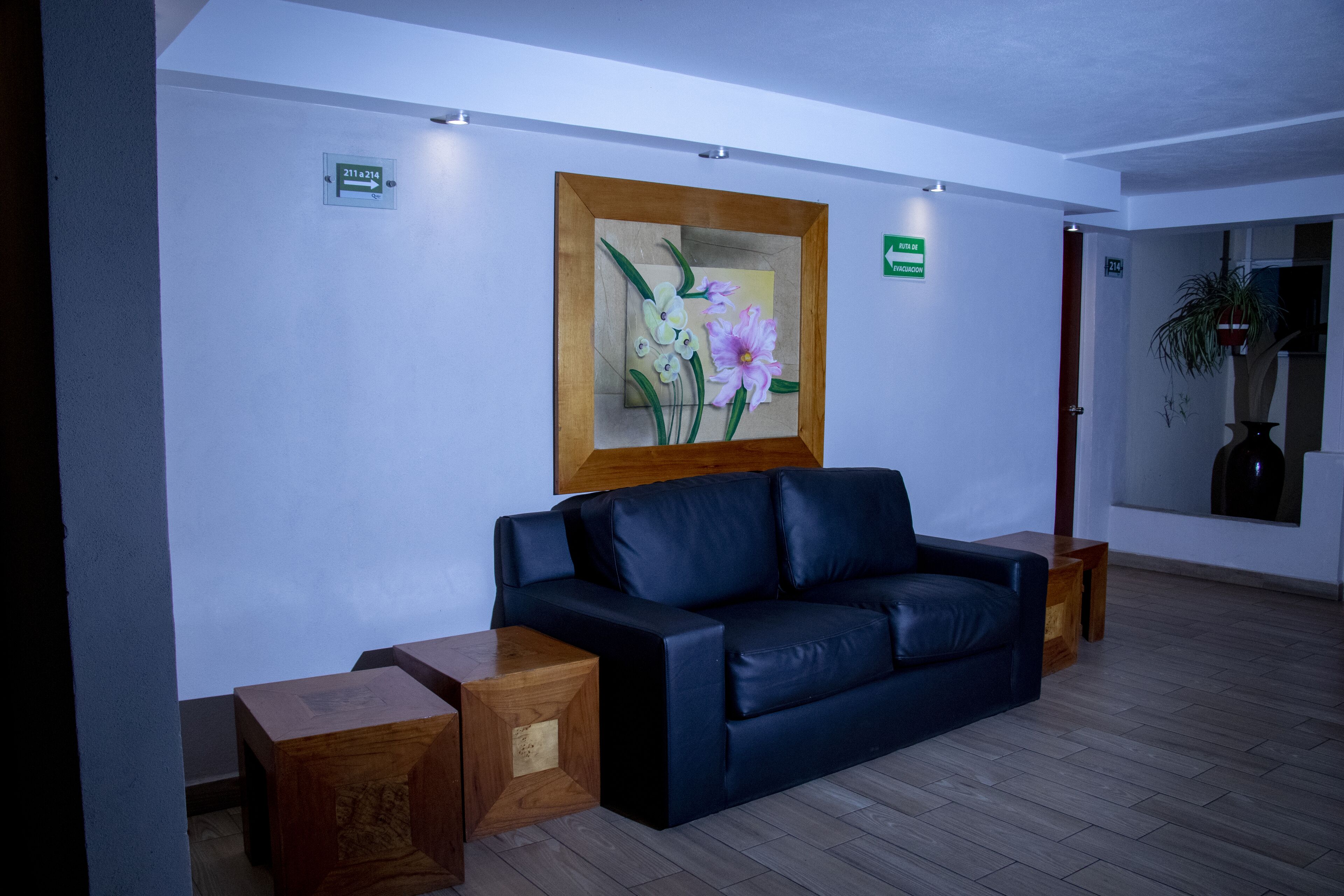 A modern lobby with a black leather sofa, wooden side tables, and a framed floral artwork on the wall.