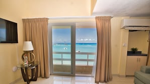 A room with a sofa, a glass table with a bottle, curtains, a TV, and a view of the ocean. - Horizon View Beach Hotel (Philipsburg)