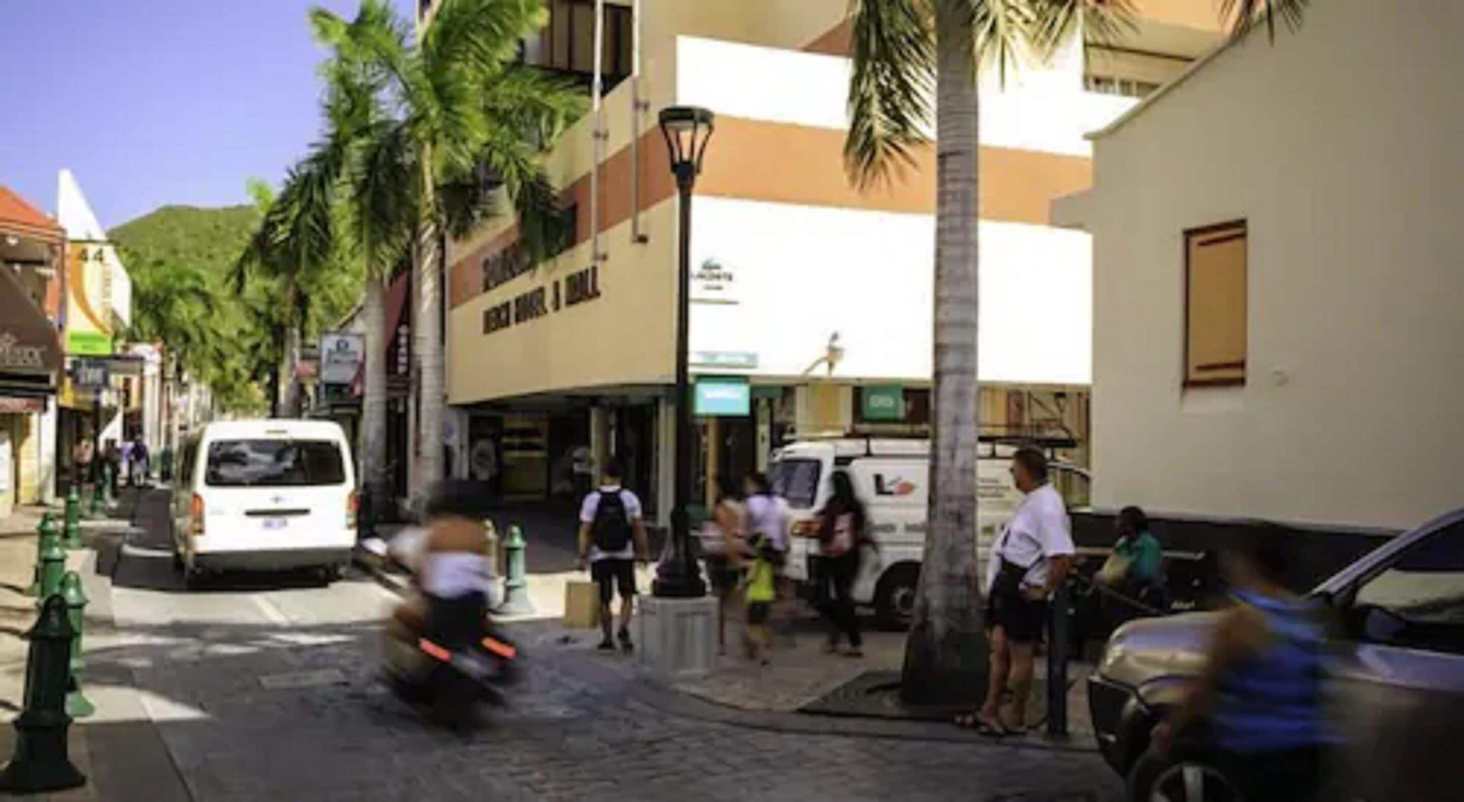 A street scene with buildings, palm trees, and people walking.