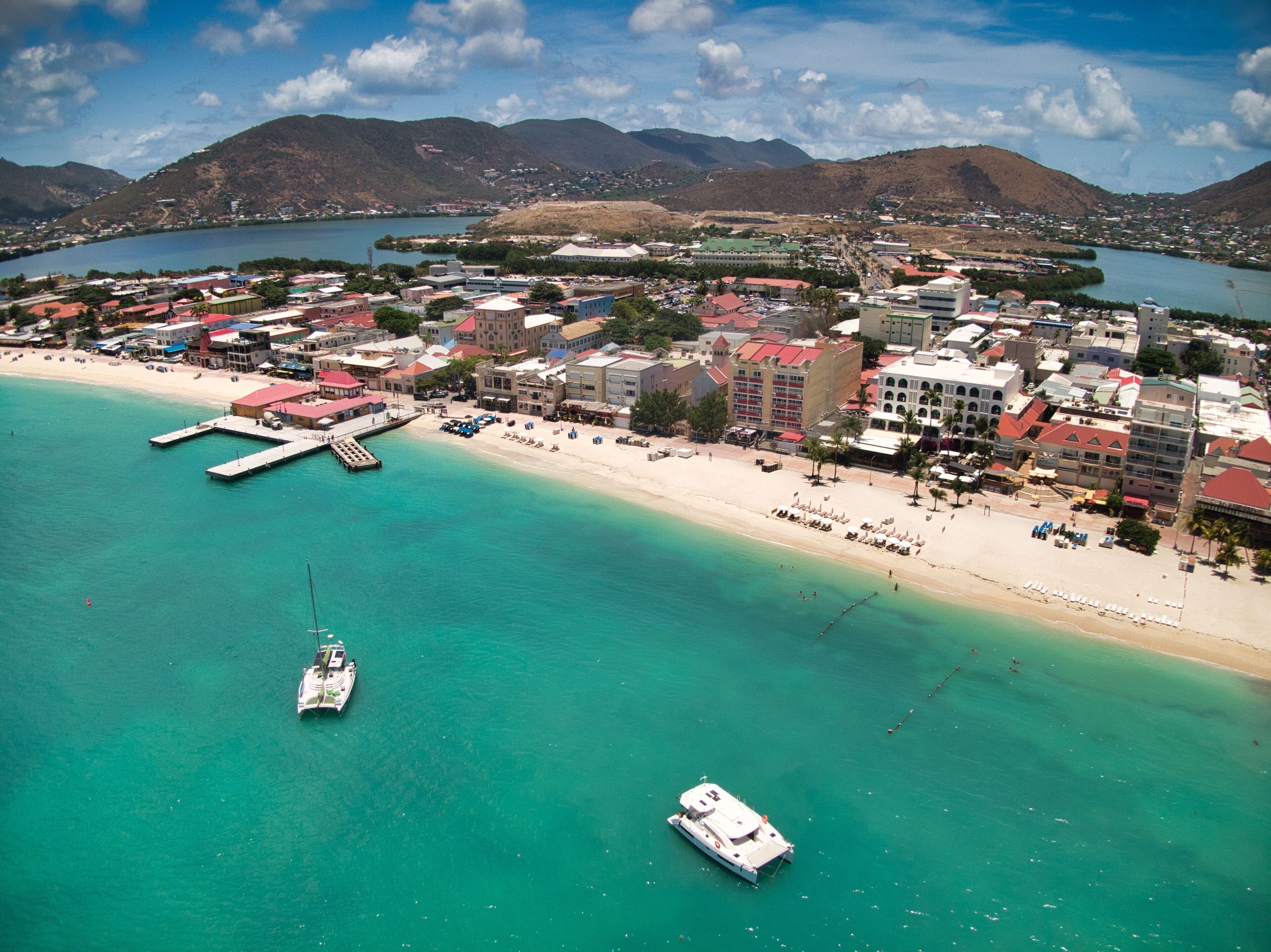 An aerial view of a coastal town with a beach, boats, and buildings.