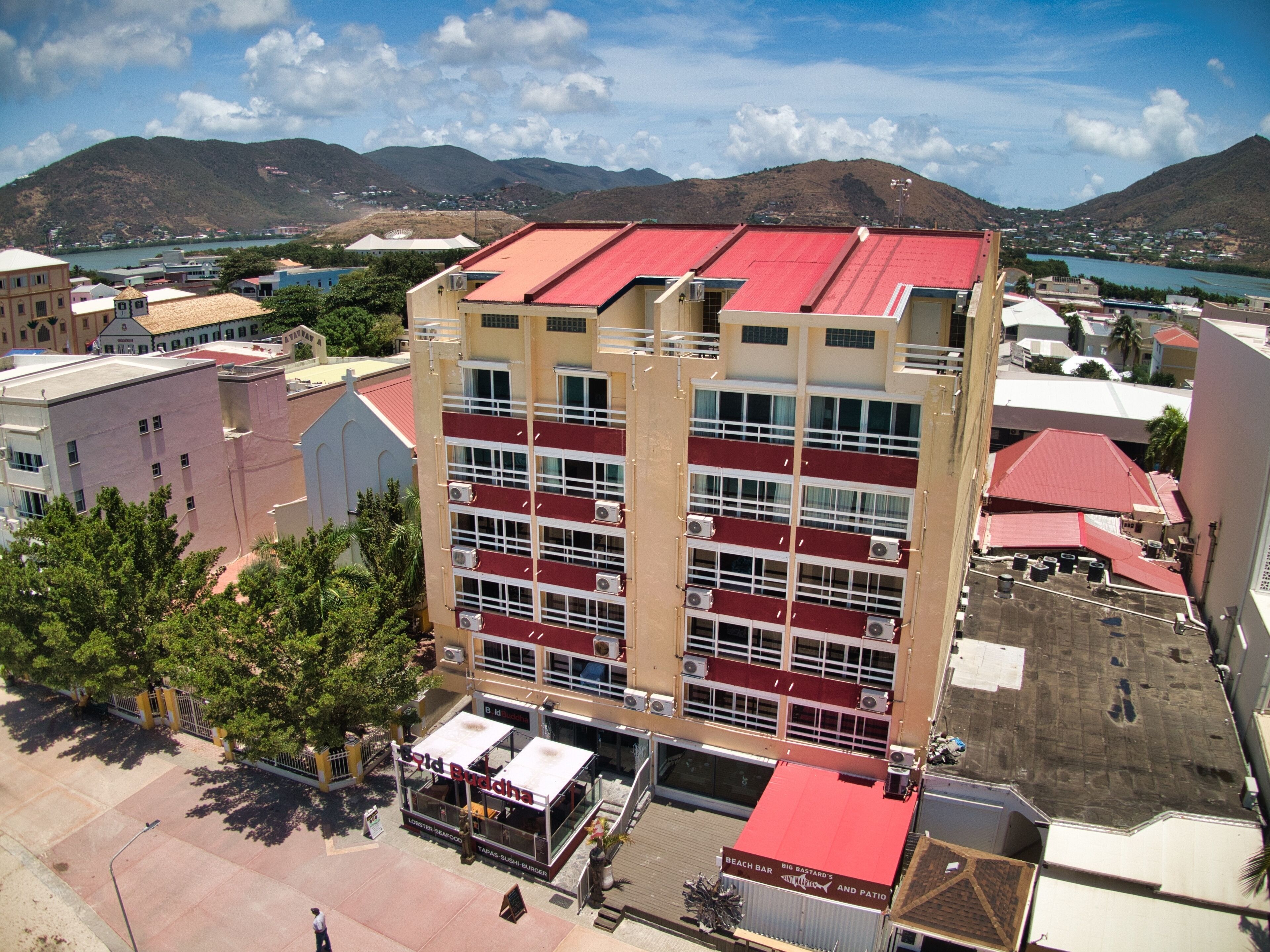 Um edifício de vários andares com telhado vermelho, próximo a um corpo d'água e montanhas.