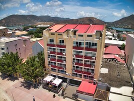 Un edificio de varios pisos con techo rojo, cerca de un cuerpo de agua y montañas.