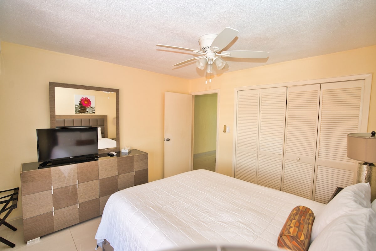 A hotel room with a bed, a TV on a dresser, a ceiling fan, and a wardrobe.