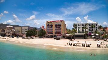 A beachside hotel with multiple floors, a sandy beach, and clear turquoise waters.