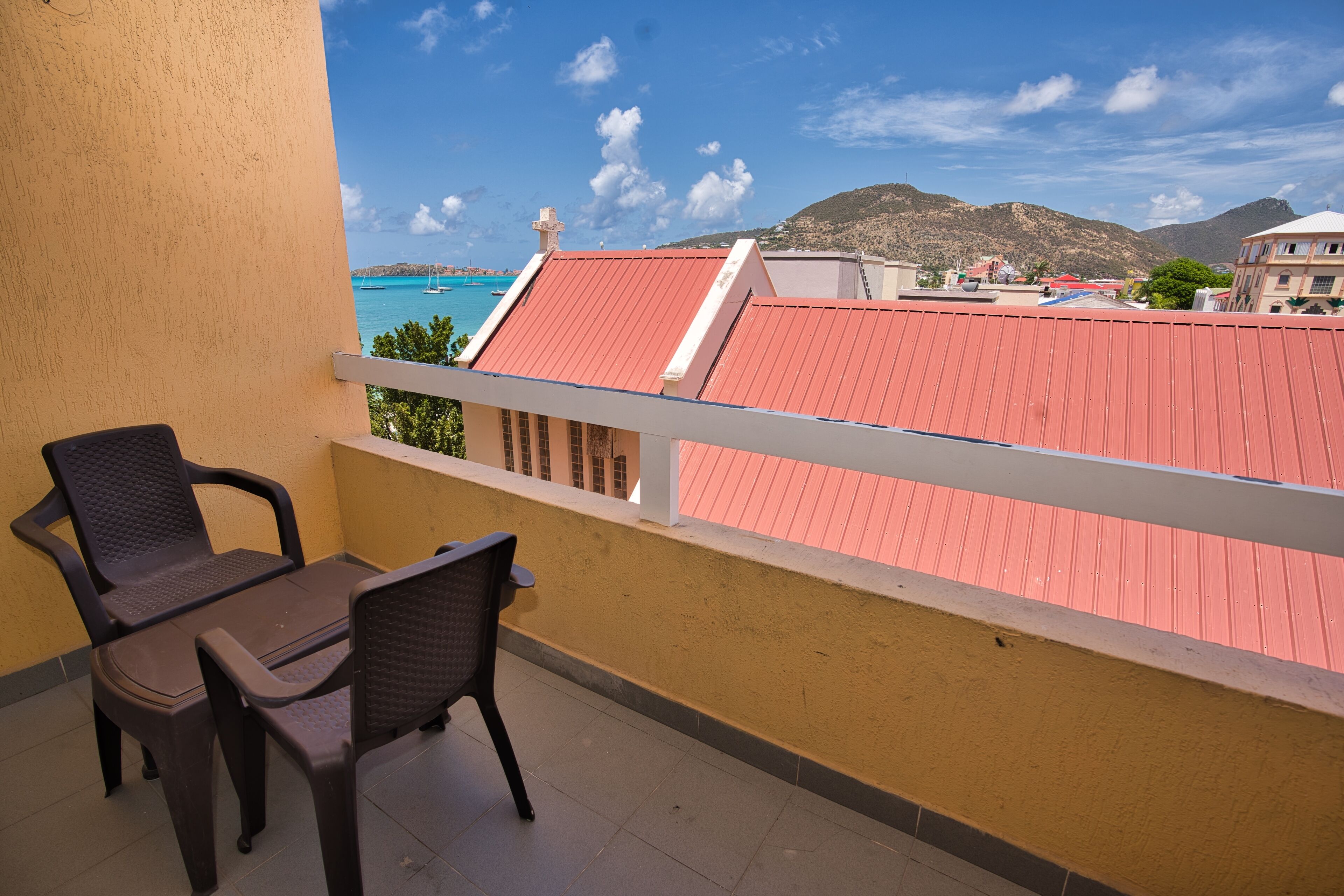 A balcony with two chairs and a table, overlooking a coastal area with buildings and mountains.