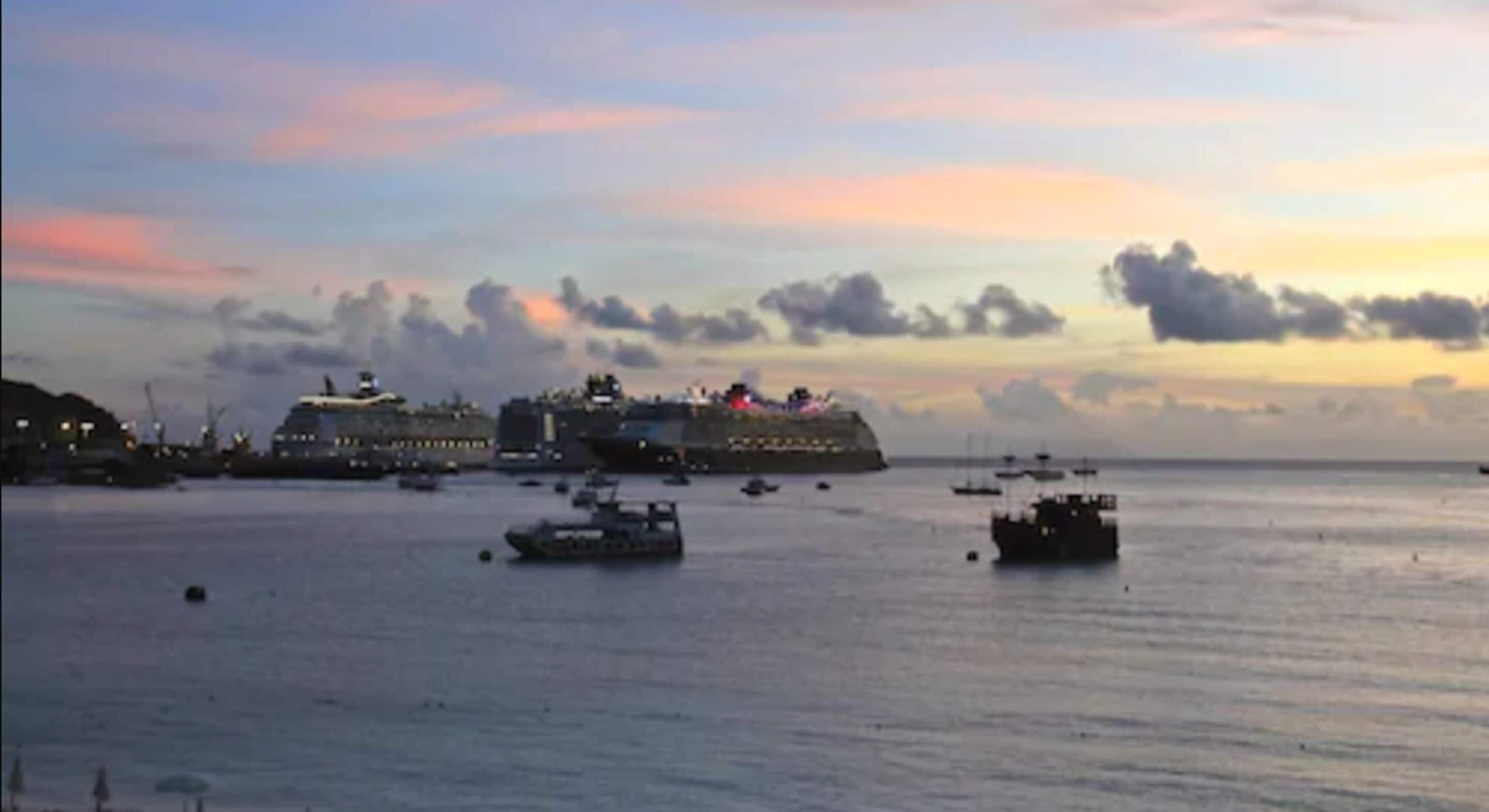 A harbor with a large cruise ship docked, surrounded by smaller boats and ships.
