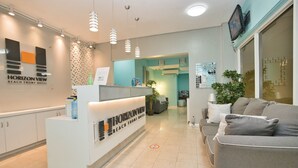 A reception area with a white counter, a grey sofa, and a TV mounted on the wall. - Horizon View Beach Hotel (Philipsburg)