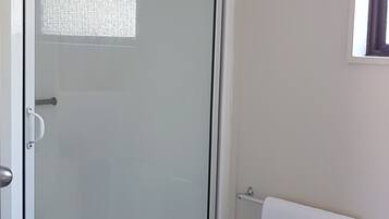 Um banheiro com divisória de chuveiro em vidro, uma toalha branca pendurada na porta e uma toalha branca em um suporte.