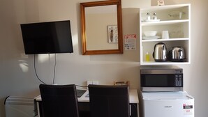 Una kitchenette equipada con microondas, tostadora y hervidor, un televisor de pantalla plana montado en la pared y una estantería con utensilios de cocina.
