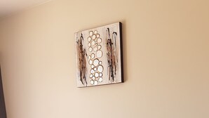 Una habitación con dos sillones grises, una mesita con mantel de encaje blanco y una obra de arte abstracto colgada en la pared.