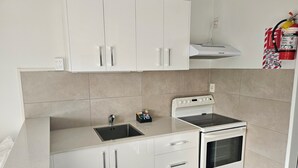 Una cocina compacta con gabinetes blancos, horno empotrado y pileta de acero inoxidable.