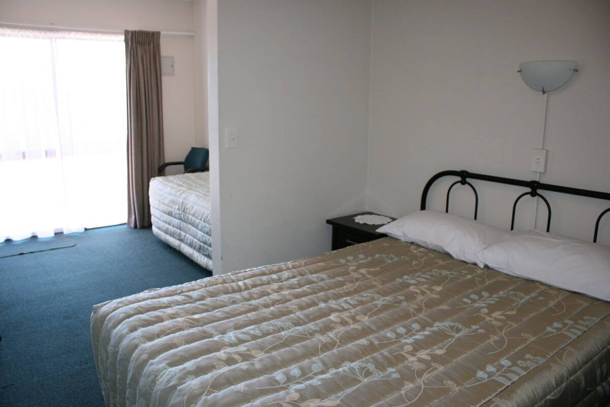 A hotel room with a single bed, a nightstand, a chair, and a window with curtains.