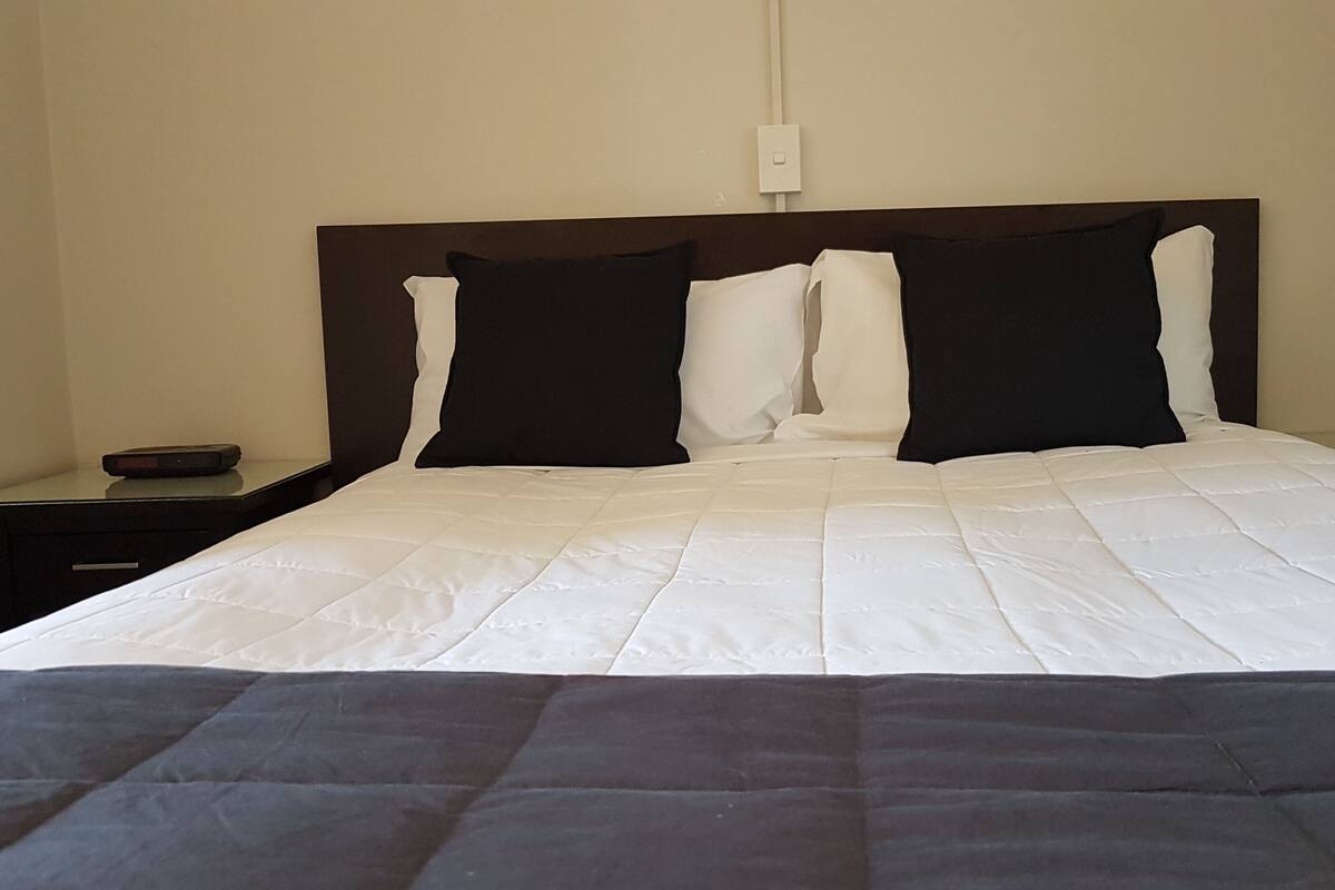 A neatly made bed with white and black bedding, a wooden headboard, and a bedside table with a lamp.