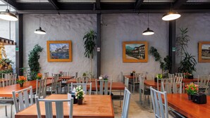 A spacious dining area with multiple tables and chairs, framed artwork on the walls, and potted plants. - Hotel Qualitel Plus (Morelia)