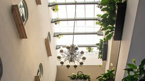 A multi-level atrium with hanging plants, a chandelier, and a view of the sky through large windows. - Hotel Qualitel Plus (Morelia)