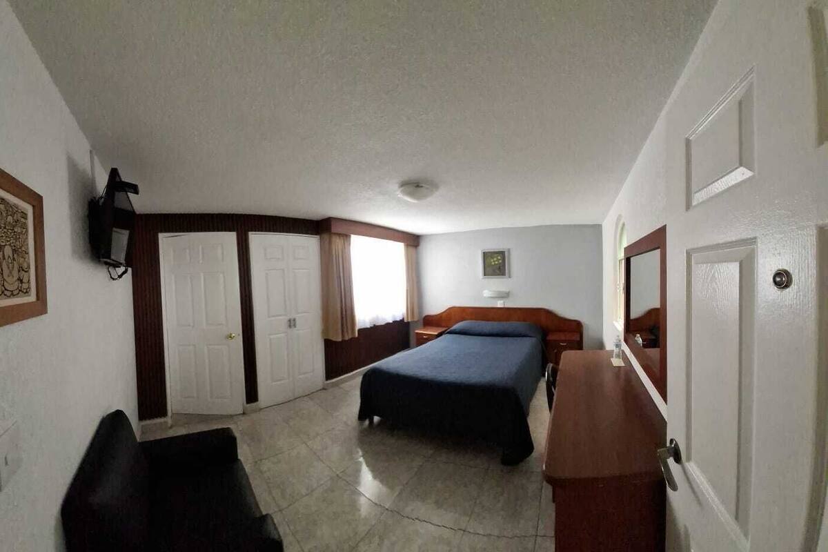 Hotellihuone, jossa on sänky, työpöytä, tuoli, vaatekaappi ja peili.