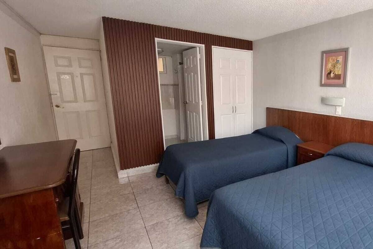 Hotellihuone, jossa on kaksi sänkyä, puinen pääty ja työpöytä sekä ovi.