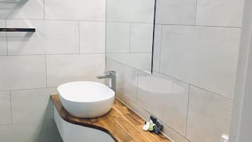 Ein modernes Badezimmer mit einem weißen Waschbecken, einer Holz-Arbeitsfläche und einem schwarzen Fliesenboden.