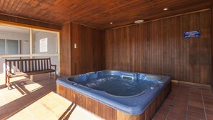 Un área de spa con suelo de madera, incluye una bañera de hidromasaje, un banco de madera y un cartel con la política de cortesía del spa.