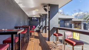 Un área de estar exterior moderna con suelo de madera y taburetes rojos acolchados.