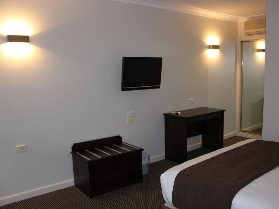 Habitación de hotel con cama, televisor montado en la pared, escritorio pequeño y espejo.