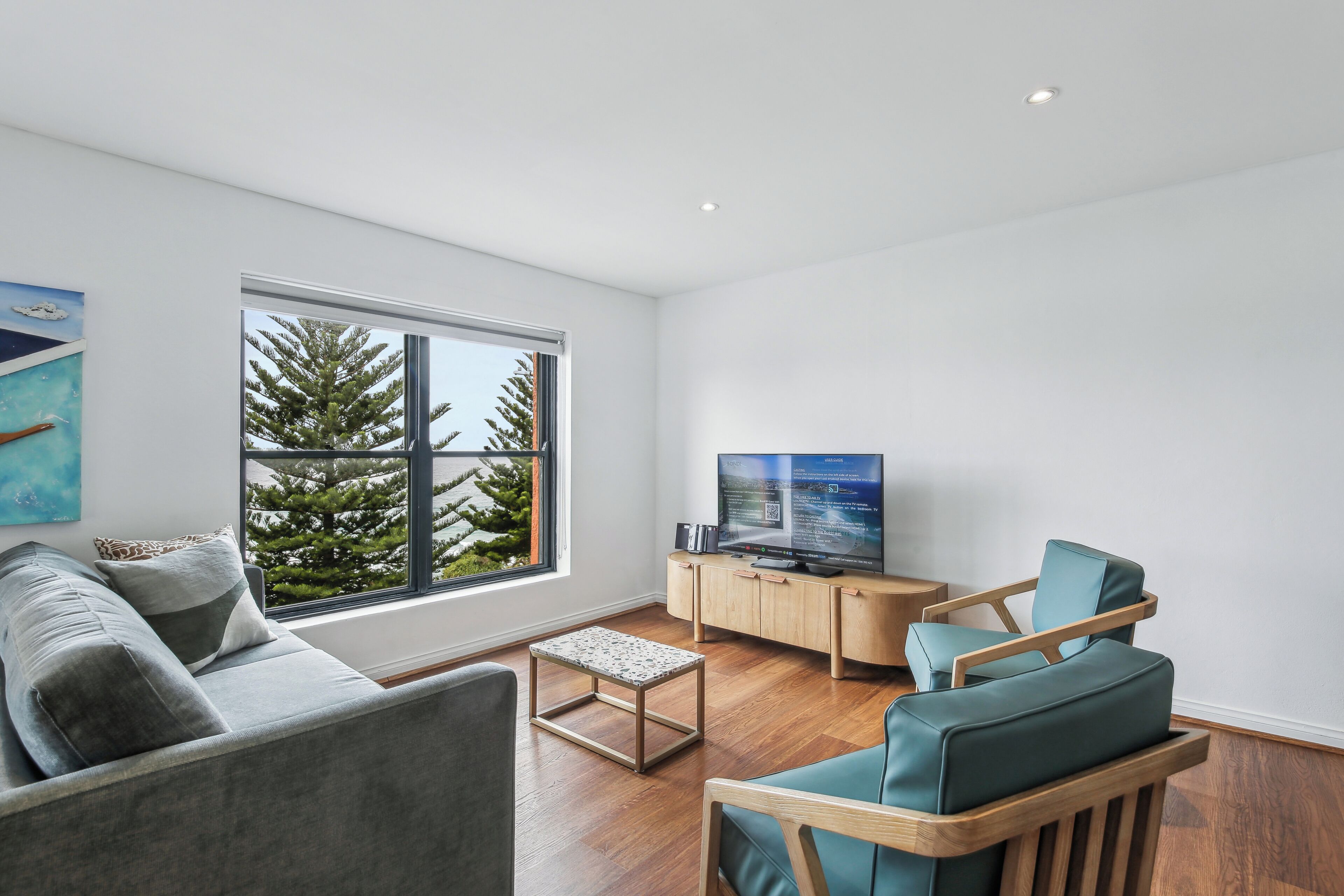 A modern living room with a sofa, a wooden chair, a small table, and a television on a wooden cabinet.