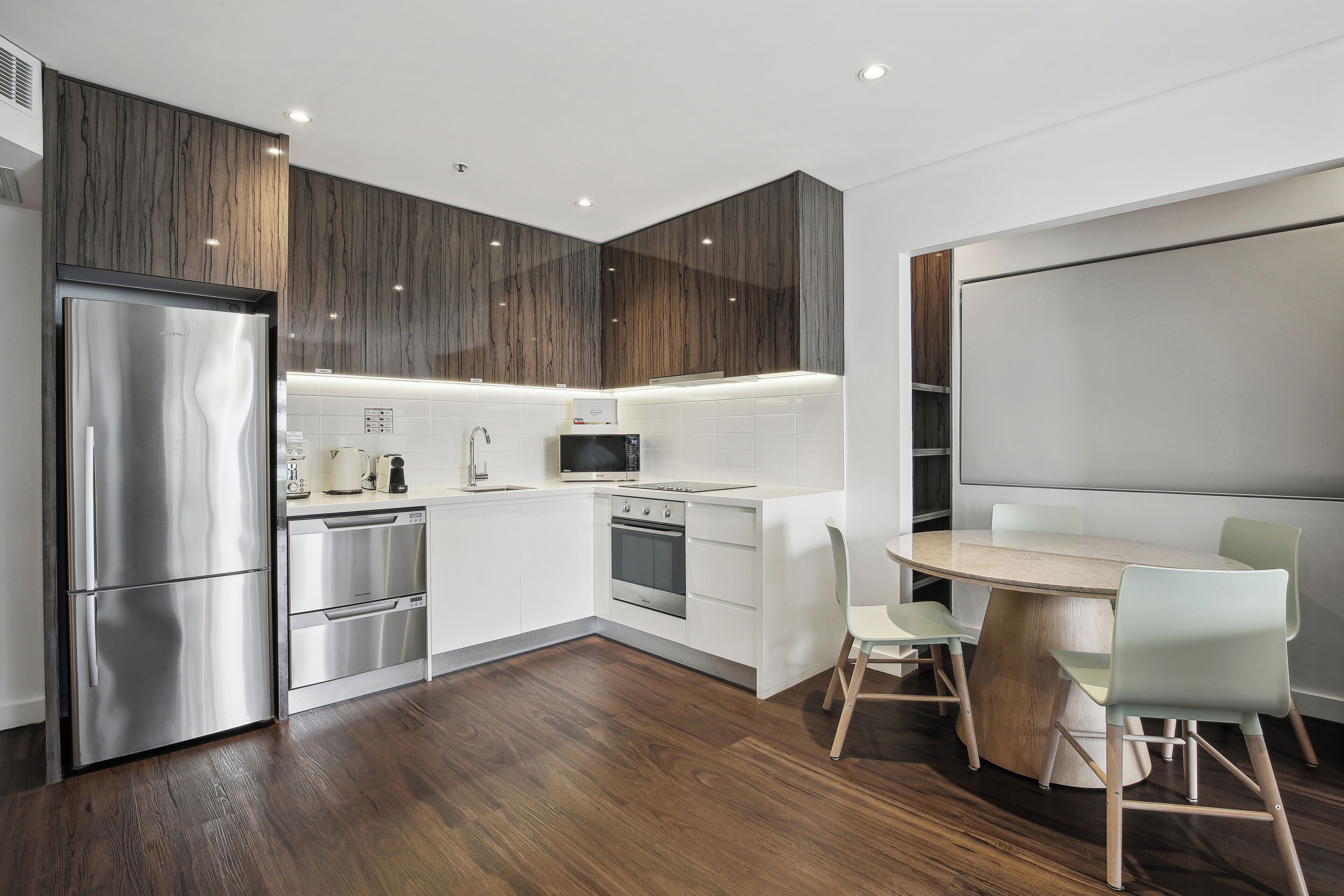 Una cocina moderna con un refrigerador de acero inoxidable, horno empotrado, microondas y una mesa de comedor de madera con sillas.