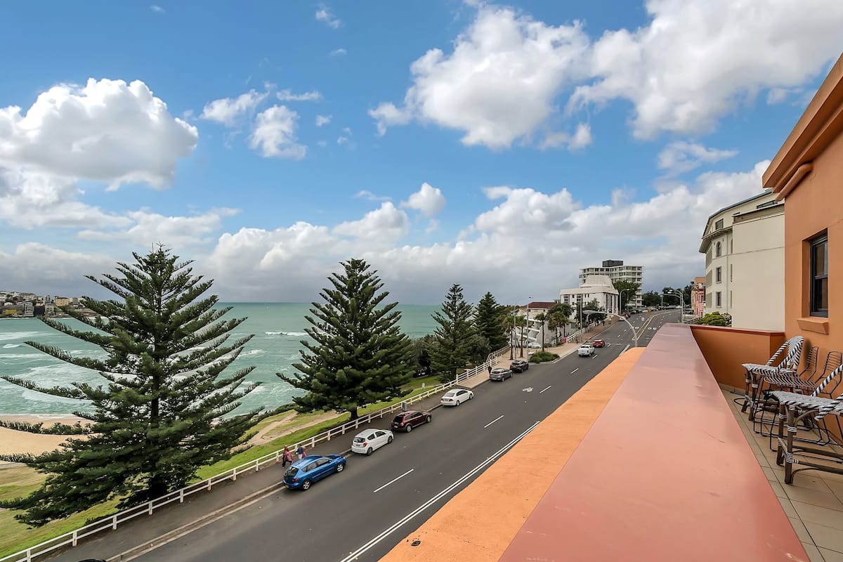 A coastal road with vehicles, a sidewalk, and a building with a balcony.